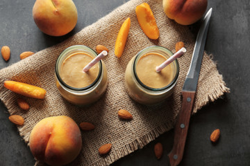 Mason jars with smoothie, peaches and napkin on grey table