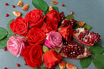 Composition of roses, pomegranate pieces and figs on color background