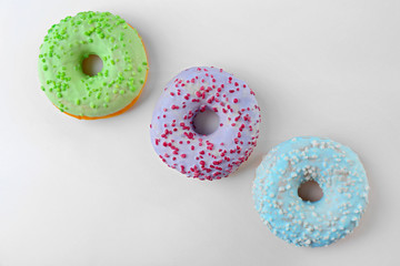 Tasty donuts with colorful sprinkles on light background