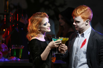 Young people in costumes drinking cocktails at Halloween party