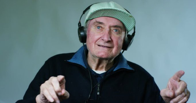 An old man listening to music with headphones and dancing by moving your hands to the beat.