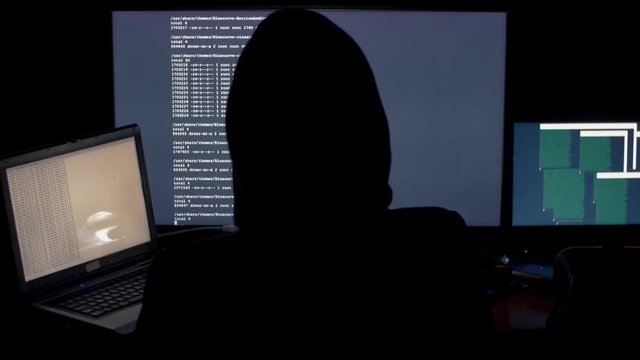 Hacker in hood cracking code using computers in dark room