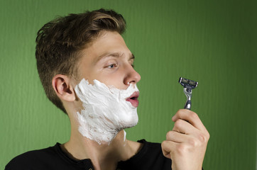 Teenager starting to shave, confused, looking at razor