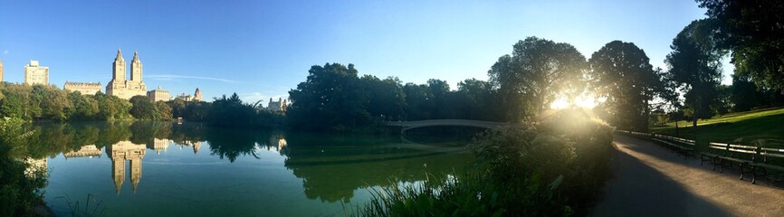Reflecting lake and Bow bridge at Central Park and the buildings with sunrise in panorama, Manhattan, New York
