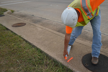 Surveyor Marking The Sidewalk While Wearing A Hard Hat And Safety Vest