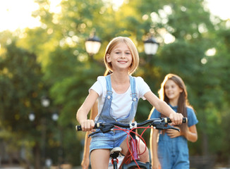 Fototapeta na wymiar Cheerful girl riding bicycle with friends in park