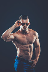  strong athletic man  in sunglasses on black background