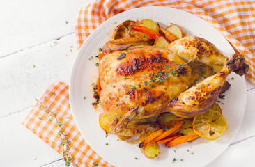 Whole roasted chicken with vegetables on  white plate.