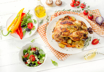 Whole roasted chicken with vegetables and salad on a white woode