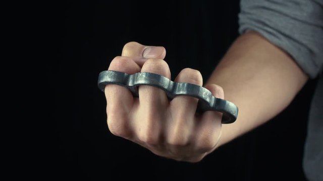 Placing knuckle-duster on the hand male fist with brass knuckles