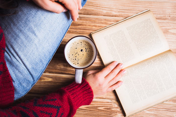 young woman in a red sweater holding a cup of coffee and reading a book