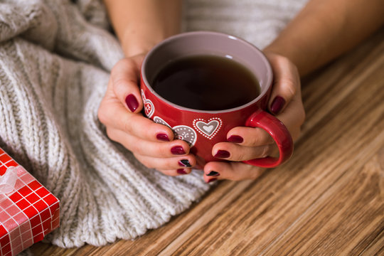 Woman with red manicure holding a red cup of tea