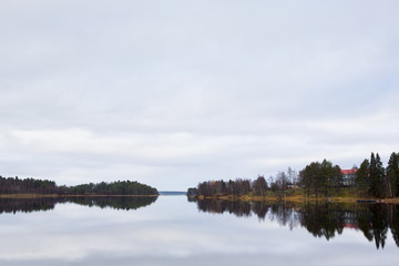 Fototapeta premium Reflective waters. Forest and building reflects from the still water.