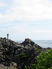 Fototapeta premium Man traveller talking on mobile phone while standing on a rock near ocean. Vancouver Island, Canada