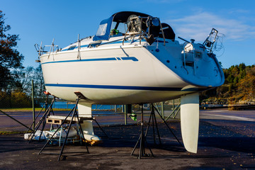Sailboat on stilts outside fenced area in port in fall.