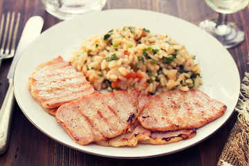 grilled meat with rice on white plate on wooden background