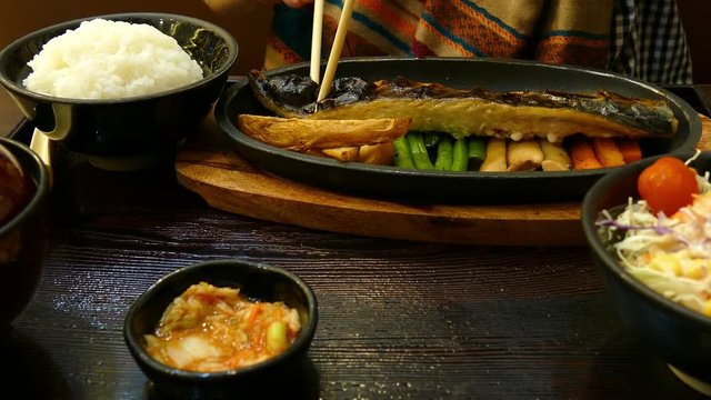 woman's hand use chopstick to pick grilled saba fish to eat with rice in japanese food set