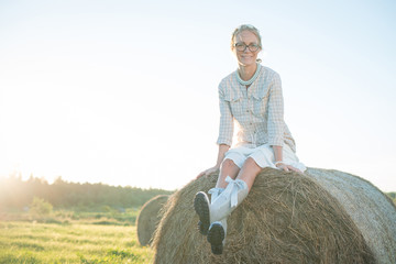 Naklejka na ściany i meble Girl in rain boots sitting on the haystack in the field