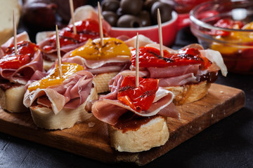 Spanish tapas with slices jamon serrano and grilled pepper. Also olives, salami, pickled onions, and peppers stuffed with cheese