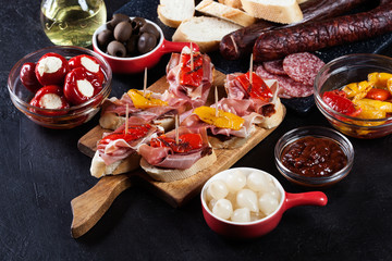 Spanish tapas with slices jamon serrano and grilled pepper. Also olives, salami, pickled onions, and peppers stuffed with cheese