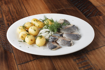 Herring fish with young potatoes balls on a white plate. wooden background.