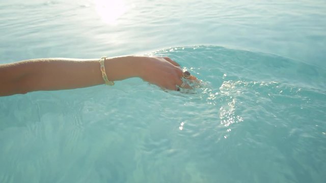 CLOSE UP: Woman sliding with fingers on smooth water surface in infinity pool