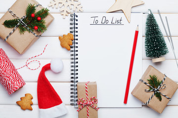 Holiday decorations, gift, present box, miniature fir tree and notebook with to do list on white wooden table from above. Christmas or winter planning concept. Flat lay style.