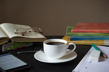 Coffee in front of textbooks,smartphone and notebook on a dark w