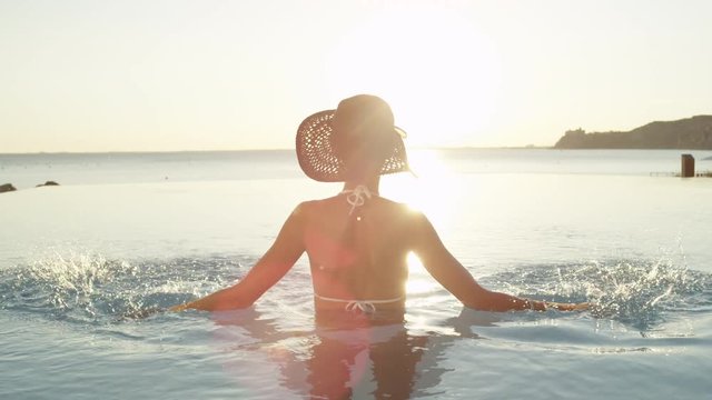CLOSE UP: Young woman in swimming pool sprinkling water at magical golden sunset