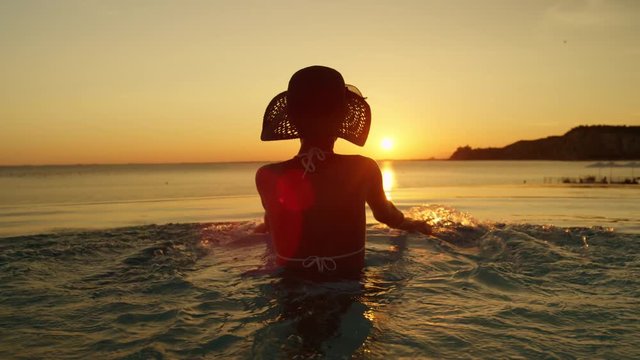 CLOSE UP: Pretty woman in swimming pool playing with water and watching sunset
