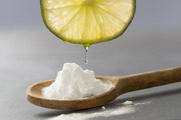 drop of juice falling from a slice of lemon in the middle of baking soda powder in wooden spoon