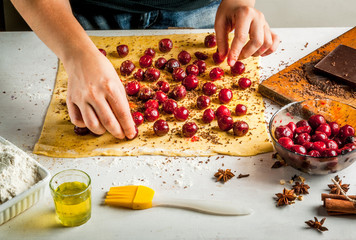 Girl is cooking strudel with chocolate and cherries, lays cherries on the dough, sprinkled with spices and chocolate. Hands in the picture