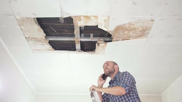 Young man call on the phone in the Service, and public utilities. Ceiling panels damaged huge hole in roof from rainwater leakage.Water damaged ceiling , Insurance case.