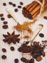 Spoonfuls of ground coffee and cinnamon, cinnamon sticks, coffee beans and star anise on the wooden background