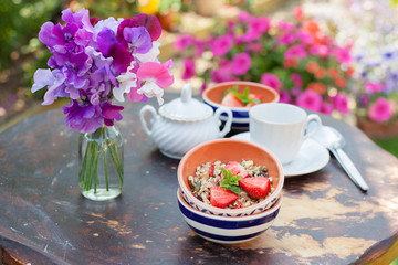 Breakfast in the garden: gluten, grain free cereals on the weathered wooden table, with white cup and saucer and sweet peas on the back, selective focus