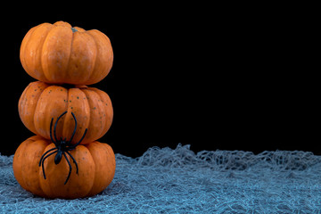 Stack of three mini pumpkins with spider and copyspace on black