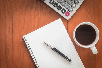 Note book with pen and a cup of coffee on wood table
