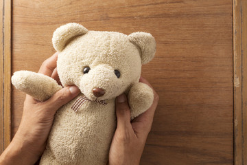 Teddy bear in hand on old wood background.