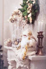 White Santa sitting on classical fireplace with golden stick under Christmas wreath. Xmas background. Winter concept.