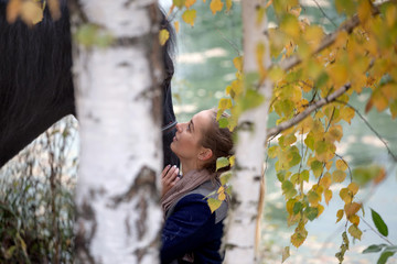 girl with a black horse in the autumn under birch