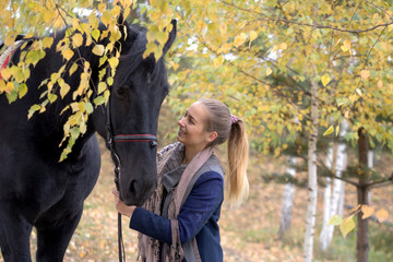 girl with a black horse in the autumn under birch