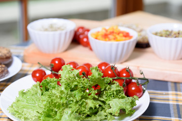 Plate with green salad, Cherry tomatoes, bowl of radish and alfalfa sprouts, paprika on a wooden cutting board. Checkered towel/pad. Delicious breakfast full of vitamins. Healthy lifestyle.