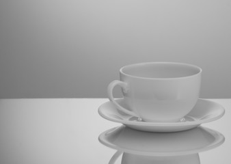 one white cup and saucer on a light background with reflection