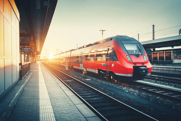 Beautiful railway station with modern high speed red commuter train at colorful sunset. Railroad with vintage toning. Train at railway platform. Industrial concept. Railway tourism