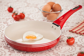 pan with fried egg and tomato on a white tablecloth