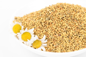 Closeup of bee pollen granules in white bowl/dish/container. Bee pollen great for immune system, energy, winter time.Daisy flower.Food ingredient for health,medical concept. Isolated,white background.