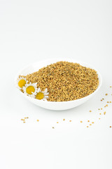 Closeup of bee pollen granules in white bowl/dish/container. Bee pollen great for immune system, energy, winter time.Daisy flower.Food ingredient for health,medical concept. Isolated,white background.