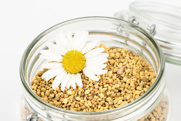 Vitamin jar for immune system, protection, energy. Get well soon. Greeting. Closeup of bee pollen granules in glass jar. Health,healthy jar. Daisy flower. Isolated,white background, copy space.