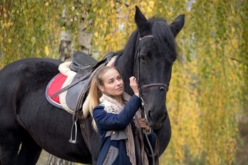 girl with a black horse in the autumn under birch