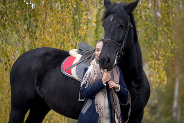 girl with a black horse in the autumn under birch